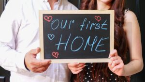 Un couple heureux tenant une pancarte en tableau noir célébrant l'achat de leur première maison ensemble.