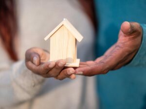 Gros plan de mains tenant une maison miniature en bois, symbolisant la propriété d'une maison et l'investissement immobilier.