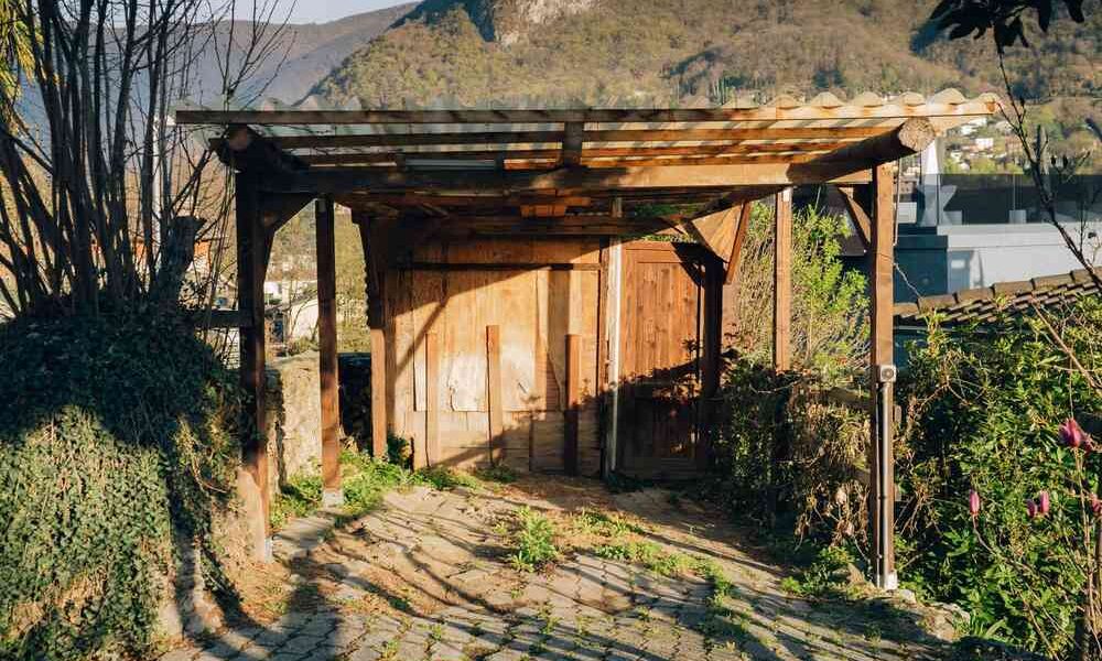 Abri en bois sur chemin de gravier, montagne derrière, végétation verte