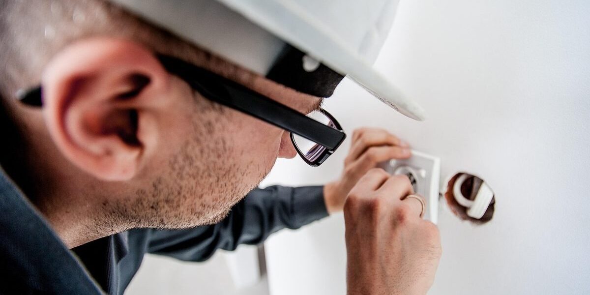 Homme en casque et lunettes manipulant un objet dans un trou de mur