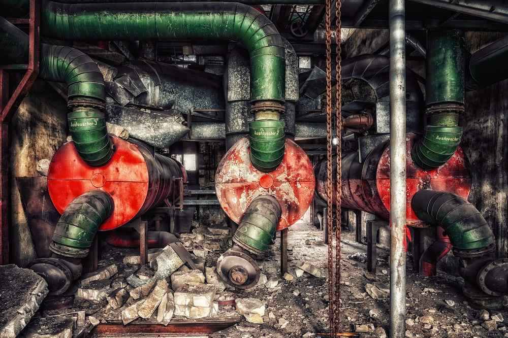 Trois tuyaux industriels rouges avec conduites vertes, dans un environnement d'usine délabré et poussiéreux