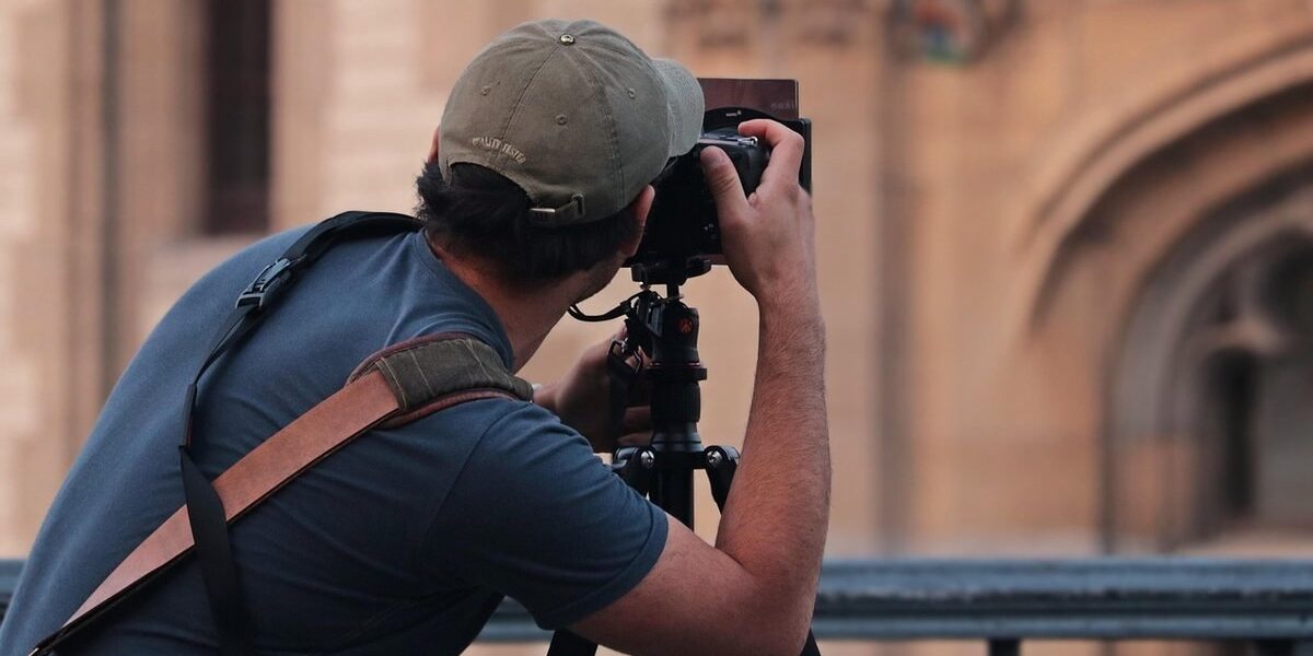 Photographe équipé d'un trépied pointant son appareil vers une façade en pierre ocre