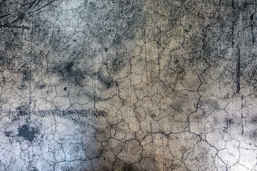 Surface fissurée, couleur grisâtre, marques sombres et craquelures visibles