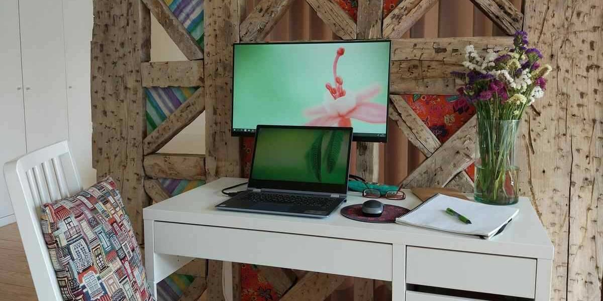 Un bureau blanc avec ordinateur, écran, chaise et vase de fleurs